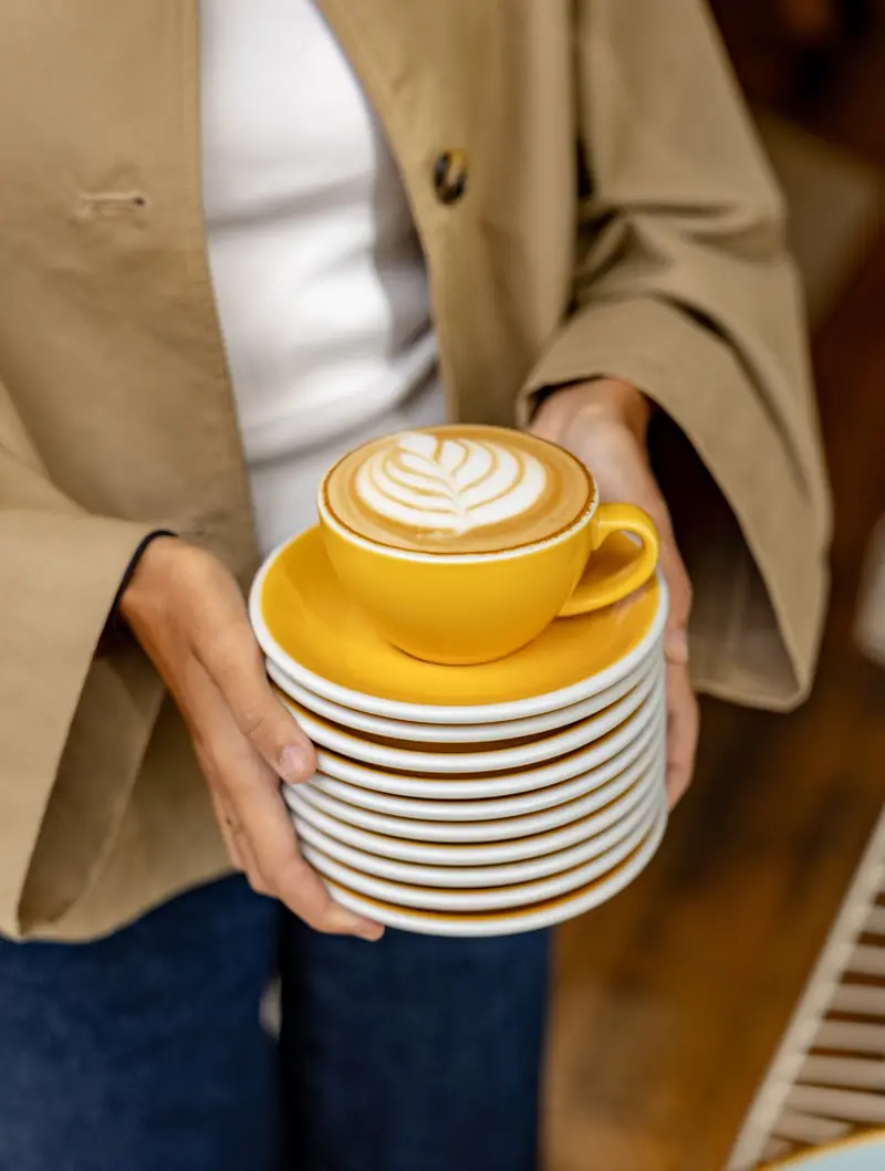 Une pile de soucoupes jaunes et un cappuccino tenus à deux mains